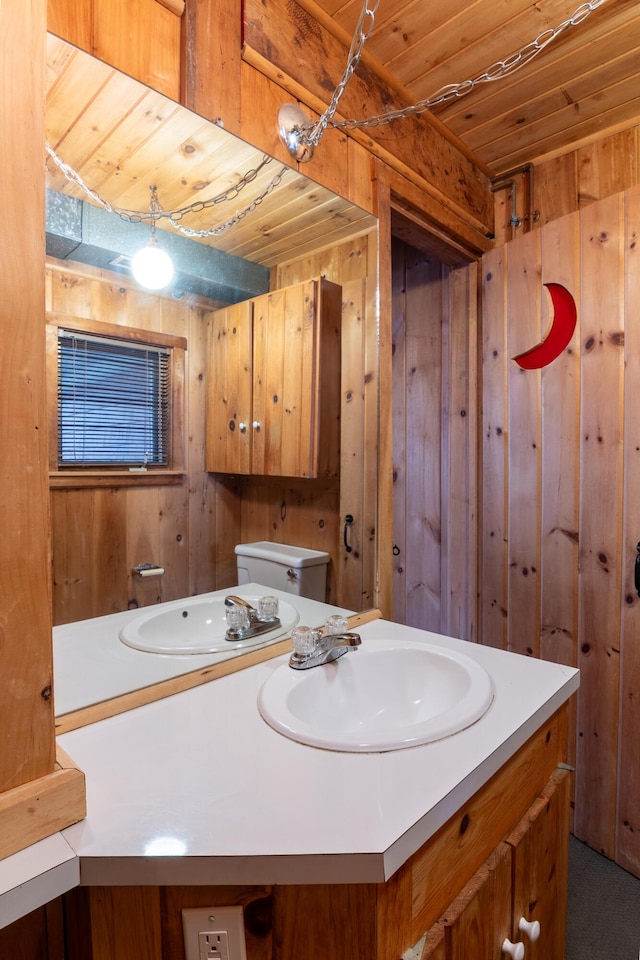 half bathroom featuring vanity, wood ceiling, wooden walls, and toilet