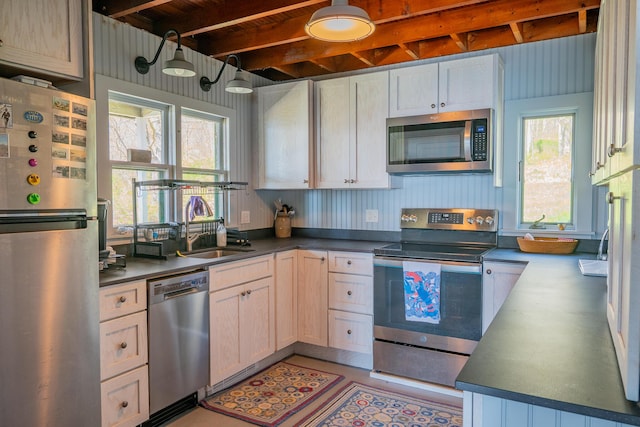 kitchen featuring stainless steel appliances, a sink, healthy amount of natural light, dark countertops, and beam ceiling