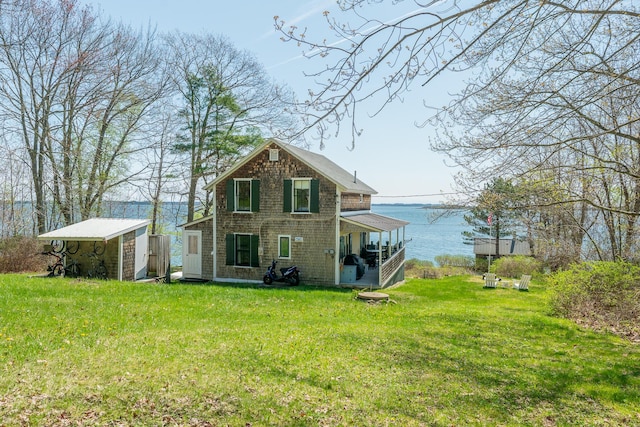 rear view of property with a lawn, an outbuilding, and a water view