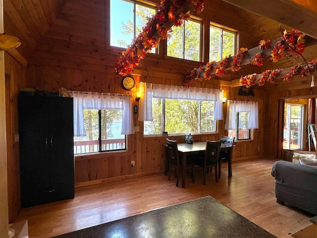 dining space featuring high vaulted ceiling, wood walls, a wealth of natural light, and wood finished floors