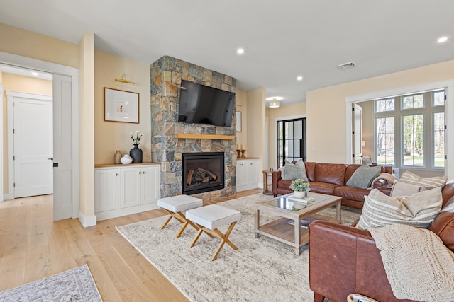 living room featuring light wood-style flooring, a stone fireplace, recessed lighting, and baseboards