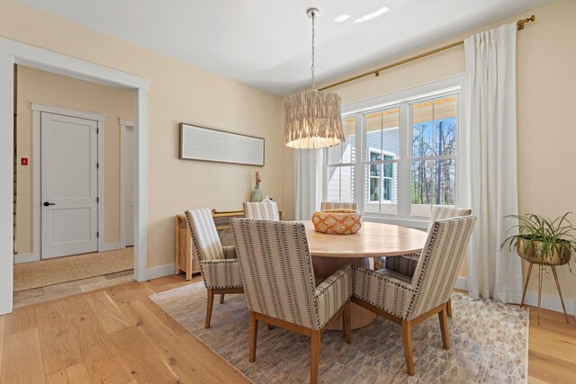 dining space with light wood-style flooring, a chandelier, and baseboards
