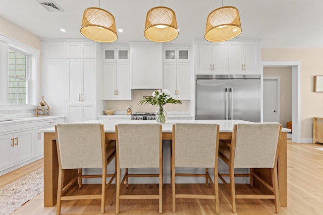 kitchen featuring stainless steel built in refrigerator, a kitchen island, light countertops, glass insert cabinets, and white cabinetry
