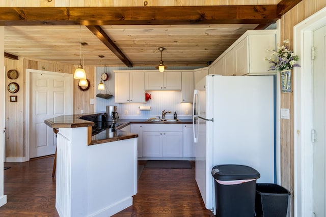 kitchen with a sink, freestanding refrigerator, dark countertops, white cabinets, and beamed ceiling