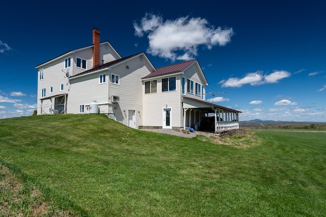 rear view of property with a lawn, a chimney, and metal roof