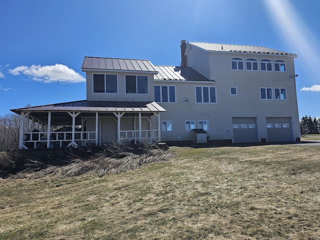 rear view of property with a lawn, an attached garage, a standing seam roof, and metal roof
