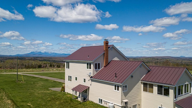 back of property featuring a standing seam roof, metal roof, a chimney, a mountain view, and a yard