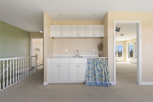 kitchen with light carpet, light countertops, white cabinetry, a baseboard heating unit, and a sink