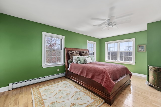 bedroom featuring a baseboard heating unit, baseboards, a ceiling fan, and wood finished floors
