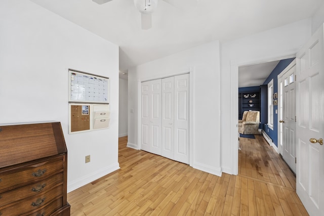 unfurnished bedroom featuring ceiling fan, a closet, baseboards, and light wood-style floors