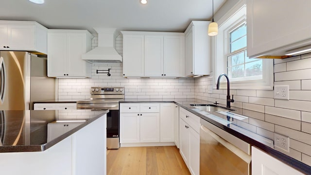 kitchen featuring pendant lighting, white cabinets, custom range hood, a sink, and appliances with stainless steel finishes