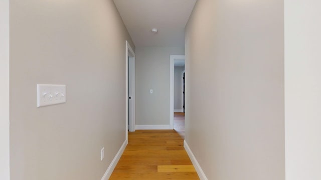 corridor with baseboards and light wood finished floors