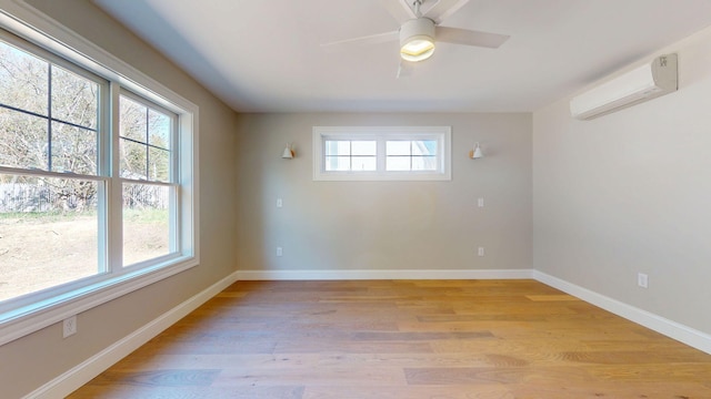 empty room with a ceiling fan, baseboards, a wall unit AC, and light wood-style floors
