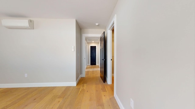 corridor featuring light wood-type flooring, a wall mounted air conditioner, and baseboards