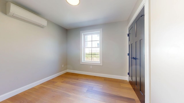 unfurnished bedroom with baseboards, a wall unit AC, light wood-style flooring, and a closet