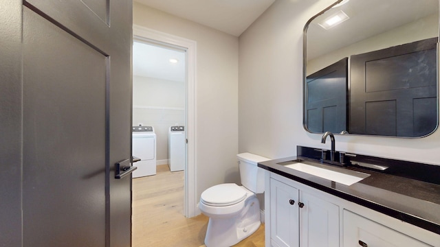 half bath with vanity, toilet, independent washer and dryer, and wood finished floors