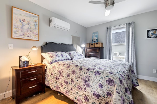 bedroom featuring baseboards, ceiling fan, a wall unit AC, and wood finished floors