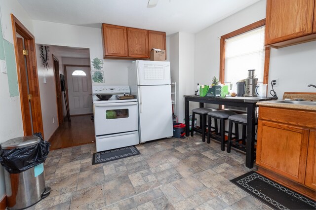 kitchen featuring white appliances, a sink, brown cabinets, stone finish flooring, and light countertops
