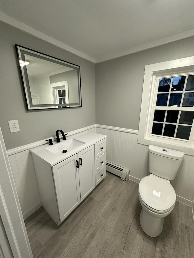 bathroom with a baseboard heating unit, wainscoting, toilet, and wood finished floors