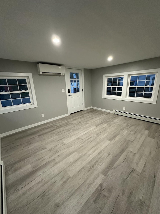 interior space featuring wood finished floors, a baseboard heating unit, recessed lighting, an AC wall unit, and baseboards