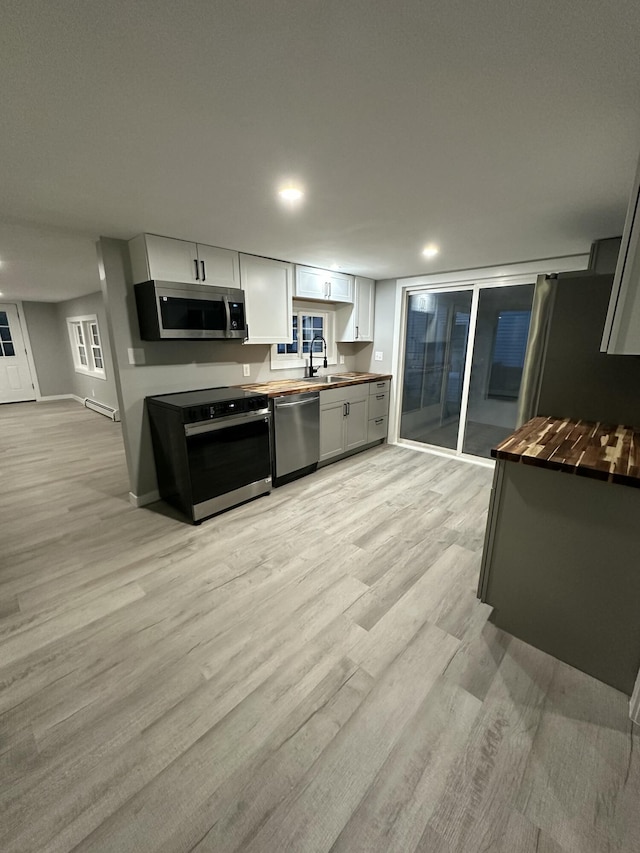 kitchen with butcher block counters, stainless steel appliances, light wood-type flooring, and a sink