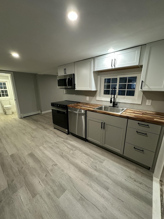 kitchen with a sink, stainless steel appliances, light wood-type flooring, baseboard heating, and butcher block counters