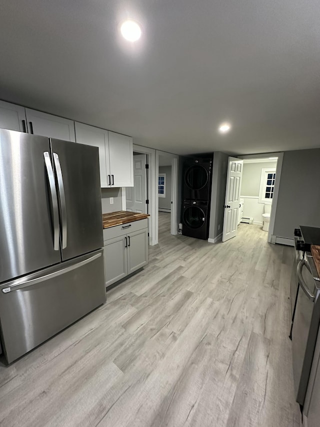 kitchen featuring light wood finished floors, stacked washer / drying machine, freestanding refrigerator, a baseboard radiator, and butcher block counters