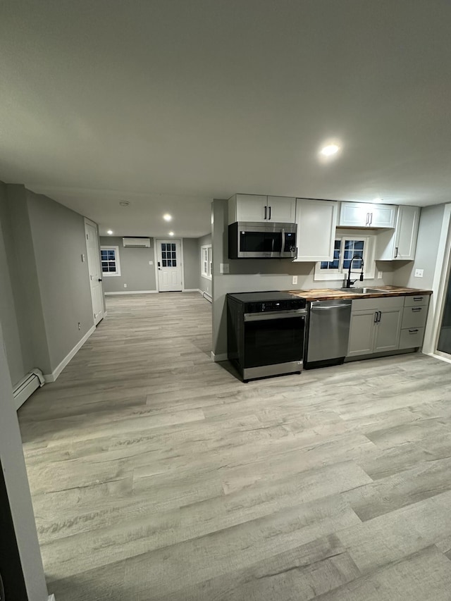 kitchen featuring a sink, stainless steel appliances, open floor plan, baseboards, and a baseboard radiator