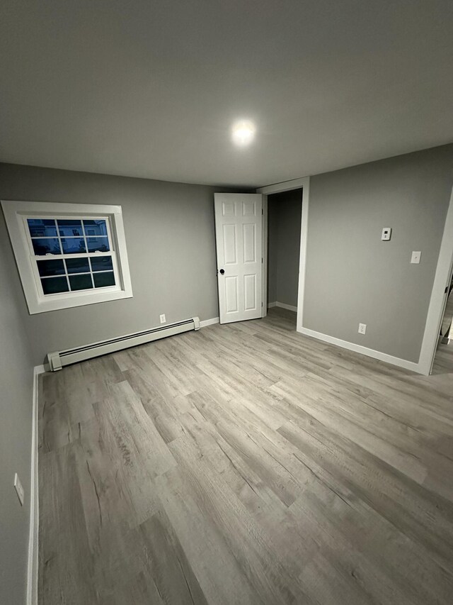 unfurnished bedroom featuring a baseboard radiator, baseboards, and wood finished floors