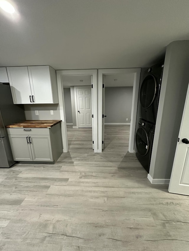 washroom featuring cabinet space, stacked washing maching and dryer, baseboards, and light wood-type flooring
