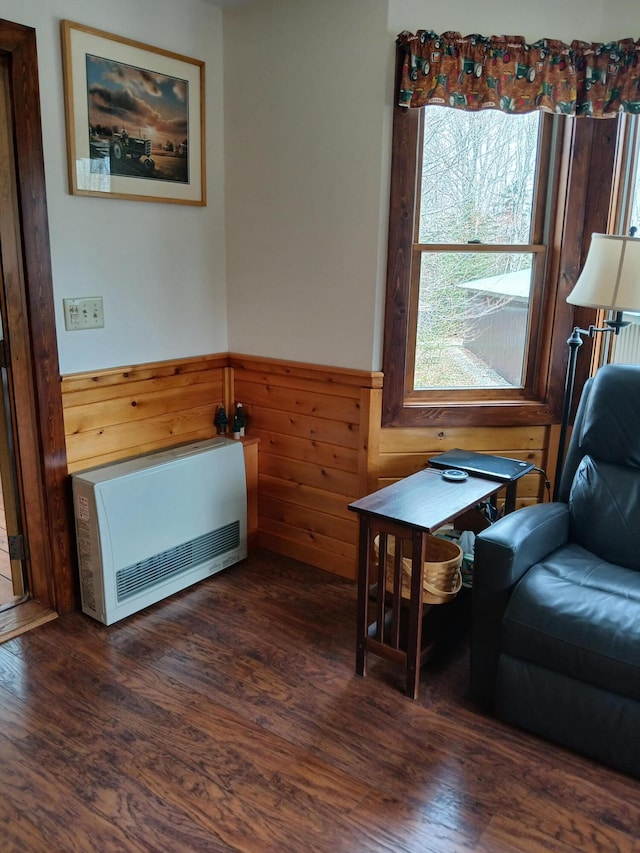 sitting room featuring heating unit, wood walls, dark wood-style flooring, and wainscoting