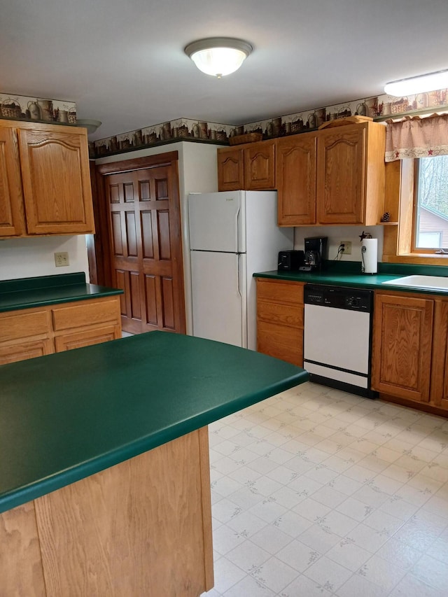 kitchen with light floors, brown cabinetry, white appliances, a sink, and dark countertops