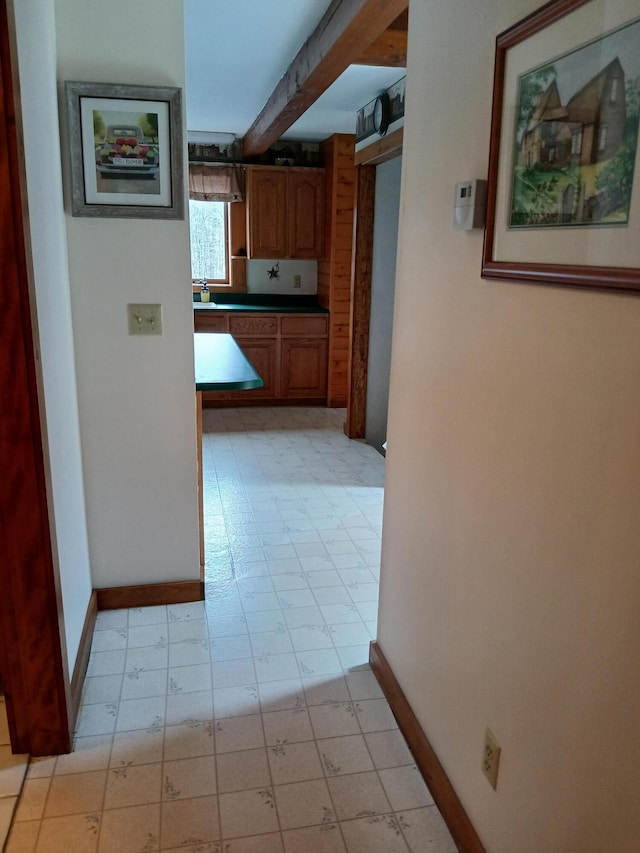 hallway with light floors, baseboards, and beam ceiling