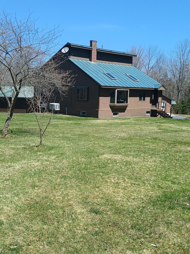 view of home's exterior with metal roof, a chimney, a lawn, and a standing seam roof