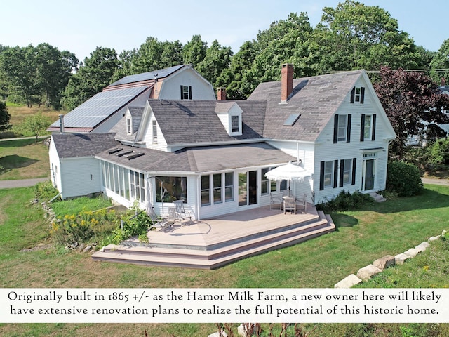rear view of property featuring roof mounted solar panels, a wooden deck, a chimney, and a yard