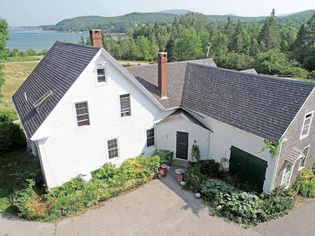 view of front of property with a wooded view, roof with shingles, and a chimney