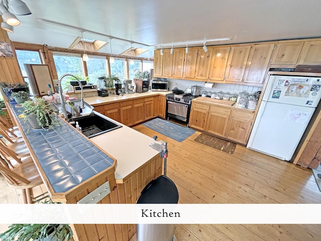 kitchen featuring track lighting, a peninsula, light wood-style floors, tile counters, and stainless steel appliances