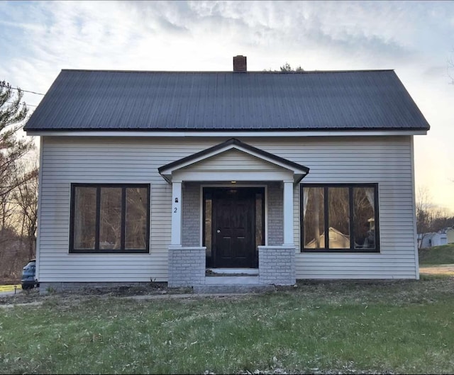 view of front of property featuring brick siding, a front lawn, a chimney, and metal roof