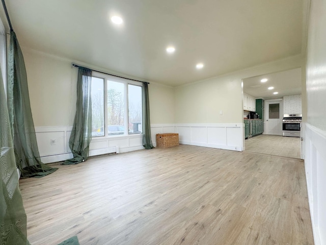 unfurnished living room with ornamental molding, wainscoting, and light wood-style flooring