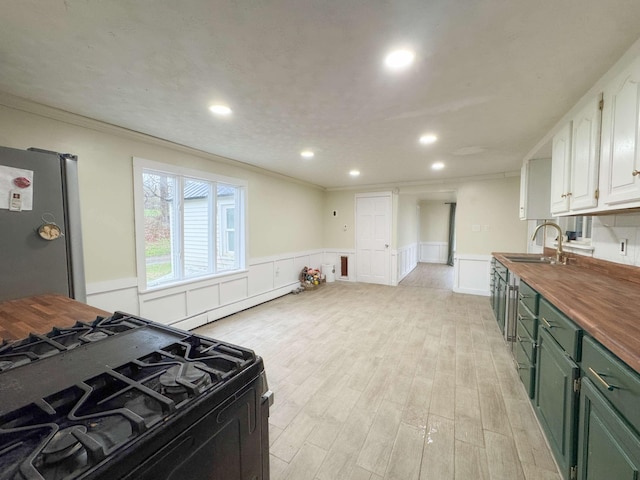 kitchen featuring gas stove, wooden counters, freestanding refrigerator, ornamental molding, and green cabinets