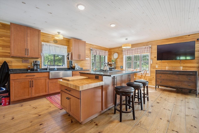 32 Whites Pond Rd, Palmyra, ME 04965 - kitchen featuring a sink, a kitchen island, light wood-style flooring, wood walls, and a breakfast bar area
