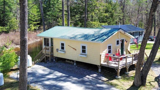 view of front of house featuring a view of trees, a wooden deck, and metal roof