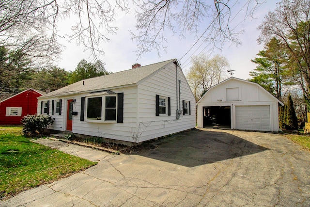 view of front of house featuring a detached garage, an outbuilding, a shingled roof, and a chimney
