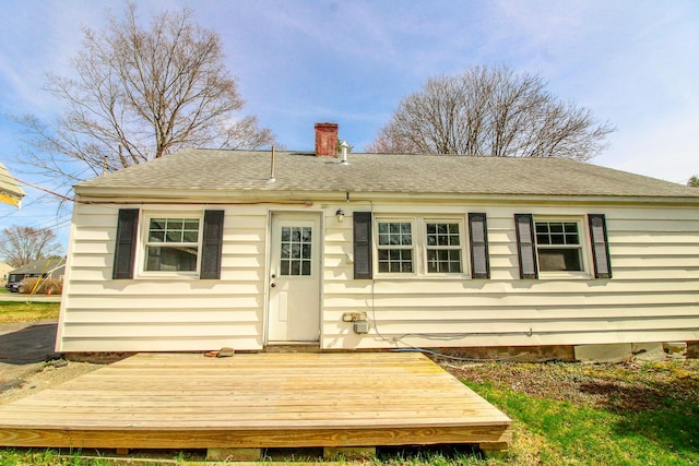 rear view of house featuring roof with shingles, a wooden deck, and a chimney