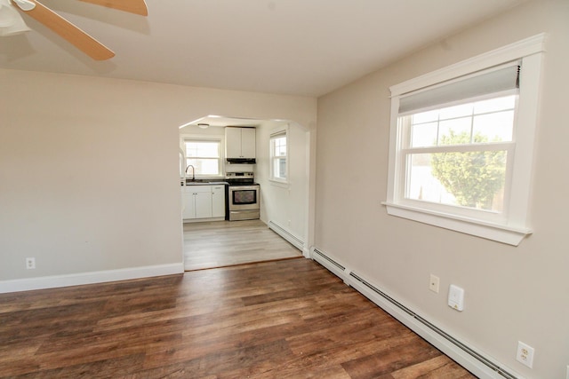 spare room with arched walkways, baseboards, baseboard heating, and wood finished floors