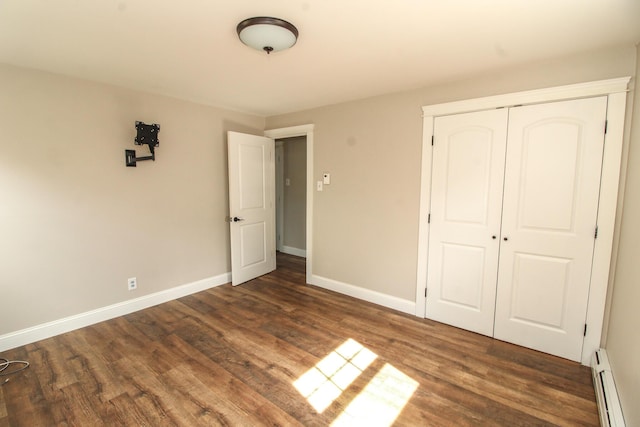 unfurnished bedroom featuring a closet, baseboards, baseboard heating, and wood finished floors