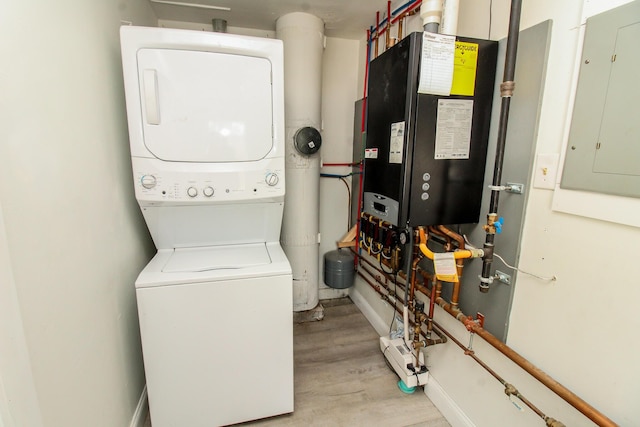 clothes washing area featuring wood finished floors, baseboards, electric panel, water heater, and stacked washer / drying machine
