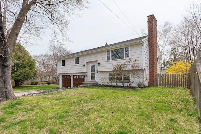 raised ranch featuring a chimney, a front yard, a garage, and fence