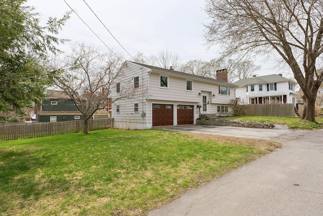 rear view of house with an attached garage, fence, driveway, and a chimney