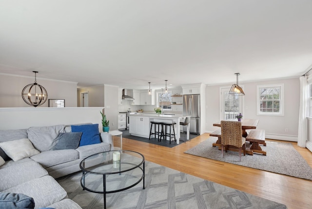living area with baseboard heating, baseboards, ornamental molding, light wood finished floors, and an inviting chandelier